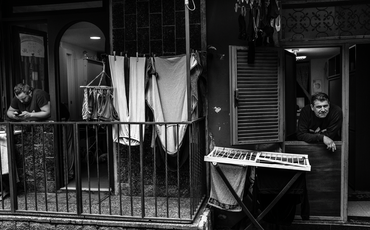 Two men lean out of the windows of the typical Neapolitan basso during the lockdown. The pandemic exacerbated social inequalities and the lockdown was experienced differently through social classes